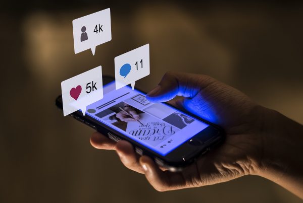 Smartphone sendo segurado por uma mão, com os ícones de seguidores, curtidas e comentários em destaque, para simbolizar o sucesso de uma campanha de marketing digital.
