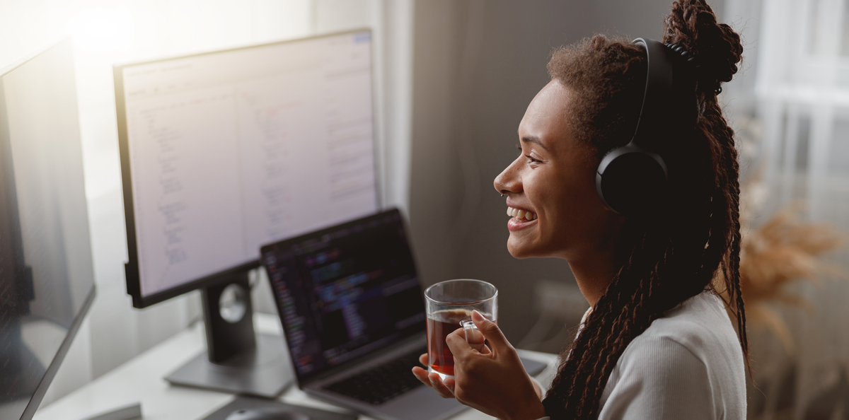 side view of cheerful young female wearing headphones and programming on computer