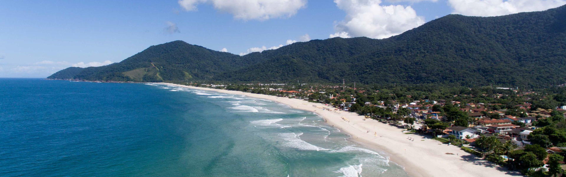 Vista aérea de praia extensa com montanhas e vilarejo